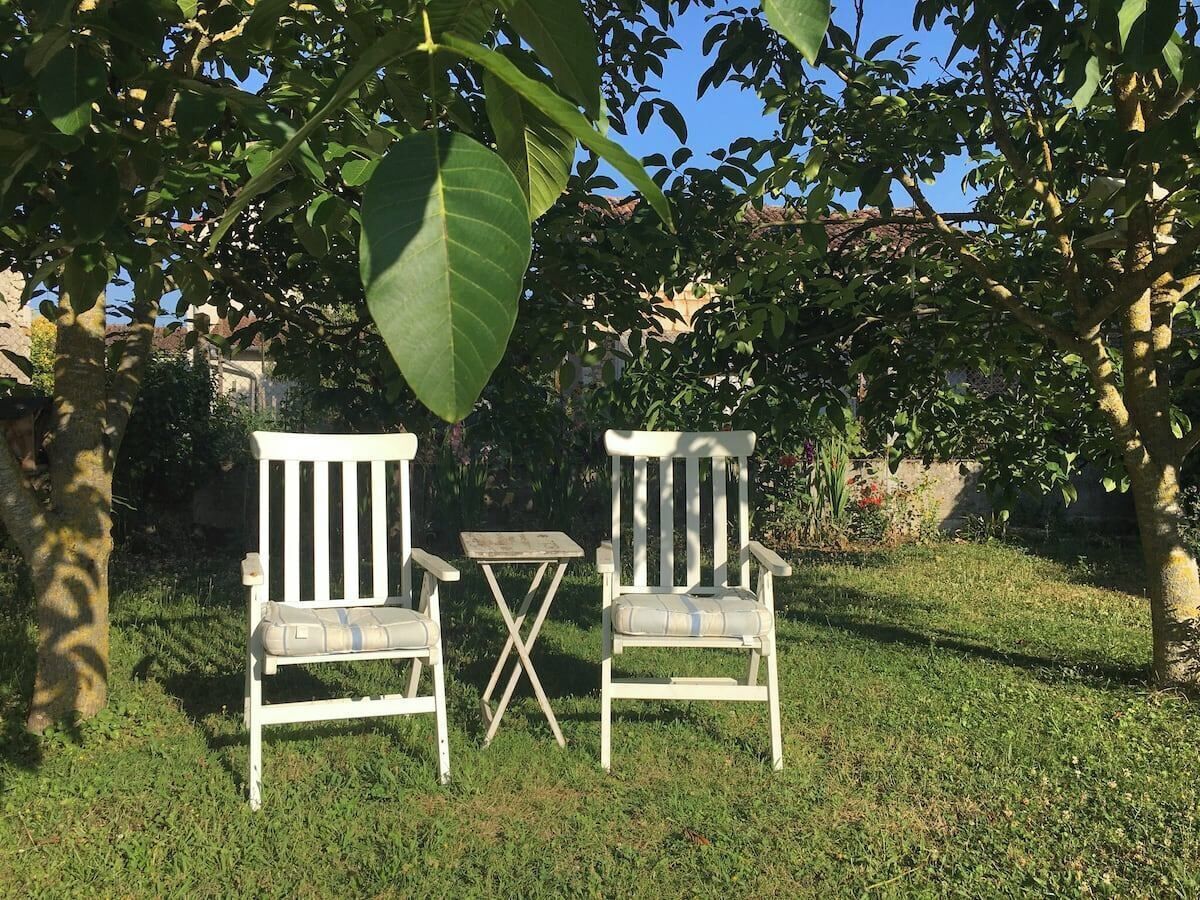 Twee witte stoelen met kussens en een klein tafeltje in een gazon met bomen.