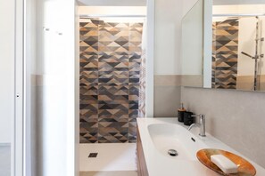 A modern bathroom with a geometric-patterned shower wall, a white sink with a soap dish, and a mirror above the sink.