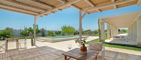 En udendørs terrasse med et træbeklædt pergola, en pool og siddepladser.