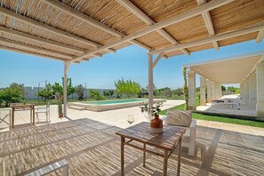 An outdoor patio with a wooden pergola, a pool, and seating areas.