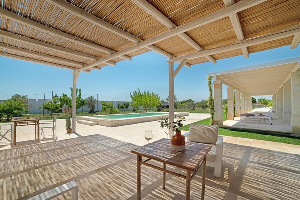 An outdoor patio with a wooden pergola, a pool, and seating areas.