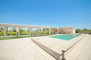 An outdoor swimming pool area with a pergola, a covered seating area, and a building with a stone facade.