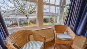 A room with two wicker chairs, a view of a river, and a window with curtains.