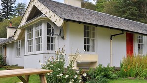 A quaint cottage with a white exterior, a red door, and a garden with various flowers.