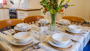 A dining table set with white plates, bowls, and cutlery, accompanied by clear glasses and a vase with flowers.