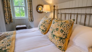 A neatly made bed with floral patterned pillows and a white comforter, a bedside table with a lamp, and a window with curtains.