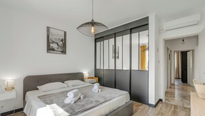 A modern bedroom with a large bed, bedside lamps, a hanging light fixture, and a framed picture on the wall.