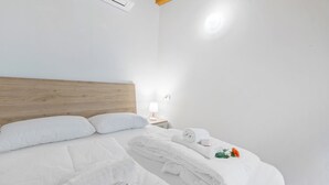 Une chambre d’hôtel avec une tête de lit en bois, du linge de lit blanc, une table de chevet avec une lampe et un petit bouquet de fleurs.
