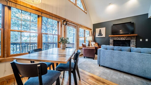 Ein geräumiges Wohnzimmer mit großem Holzesstisch, blau gepolsterten Stühlen, einem grauen Sofa und einem Kamin aus Stein.