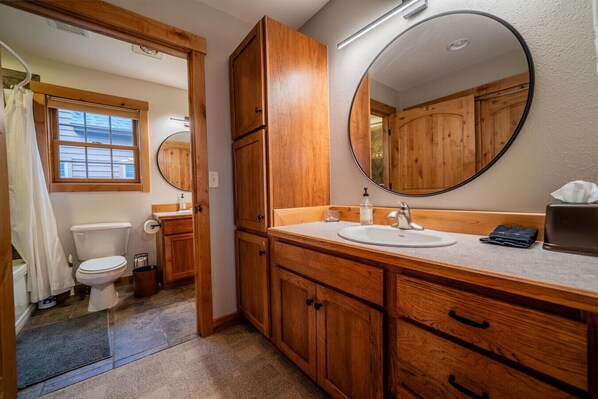 A bathroom with wooden cabinets, a sink, a mirror, and a toilet.