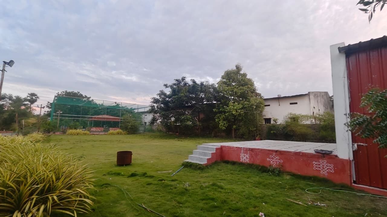 Un espacio exterior con césped, un edificio rojo, una escalera y una estructura verde al fondo.