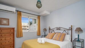 Un dormitori amb un llit, dues taules de nit, un armari i una finestra amb cortines, a més d'un aparell d'aire condicionat.