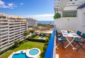 Un balcón con mesa y sillas, piscina y vistas al mar y edificios.