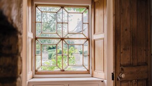 A bay window with a geometric design, wooden door, and a view of greenery outside. - Historic 3 BD Cottage in the Cotswolds (Milton-under-Wychwood)