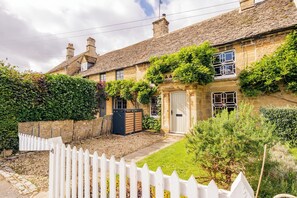 A stone house with a white picket fence, a well-maintained garden, and a clear sky. - Historic 3 BD Cottage in the Cotswolds (Milton-under-Wychwood)