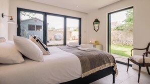 A bedroom with a large bed, a chair, and a view of the outside. - Historic 3 BD Cottage in the Cotswolds (Milton-under-Wychwood)