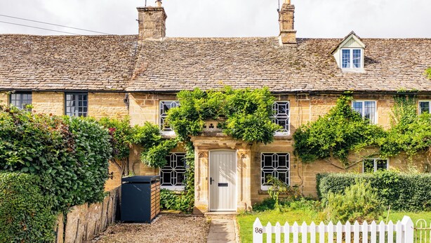 A traditional stone house with a tiled roof, a white picket fence, and a well-maintained garden. - Historic 3 BD Cottage in the Cotswolds (Milton-under-Wychwood)