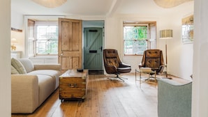 A cozy room with a wooden floor, a beige sofa, a leather armchair, and a vintage trunk. - Historic 3 BD Cottage in the Cotswolds (Milton-under-Wychwood)