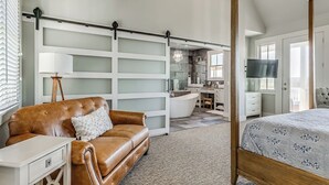 A bedroom with a four-poster bed, a brown leather sofa, a desk, and a large mirror. - Shore Enough | Carlton Landing Lakeview, Up to 18 (Eufaula)