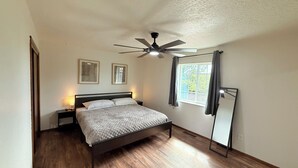 A bedroom with a bed, a ceiling fan, two bedside lamps, a window with curtains, and a wall-mounted mirror. - 3Br Farmington Home & 75” Smart Tv + Pet Friendly (Farmington)