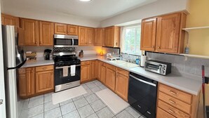 A modern kitchen with wooden cabinets, stainless steel appliances, and a window providing natural light. - 3Br Farmington Home & 75” Smart Tv + Pet Friendly (Farmington)