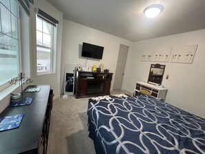 A bedroom with a bed, a dresser, a TV, and a window.