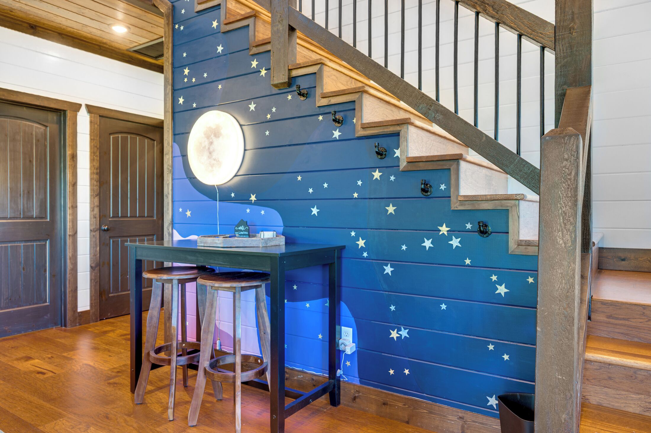 Una escalera con una pared azul decorada con estrellas y una luna, que lleva a una plataforma con una mesa y taburetes.
