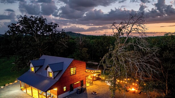 A rustic cabin with a sloped roof, a porch, and a well-lit interior. - Stargazing Dome, Hot Tub, Fire Pit, Luxury Cabin near Broken Bow (Broken Bow)