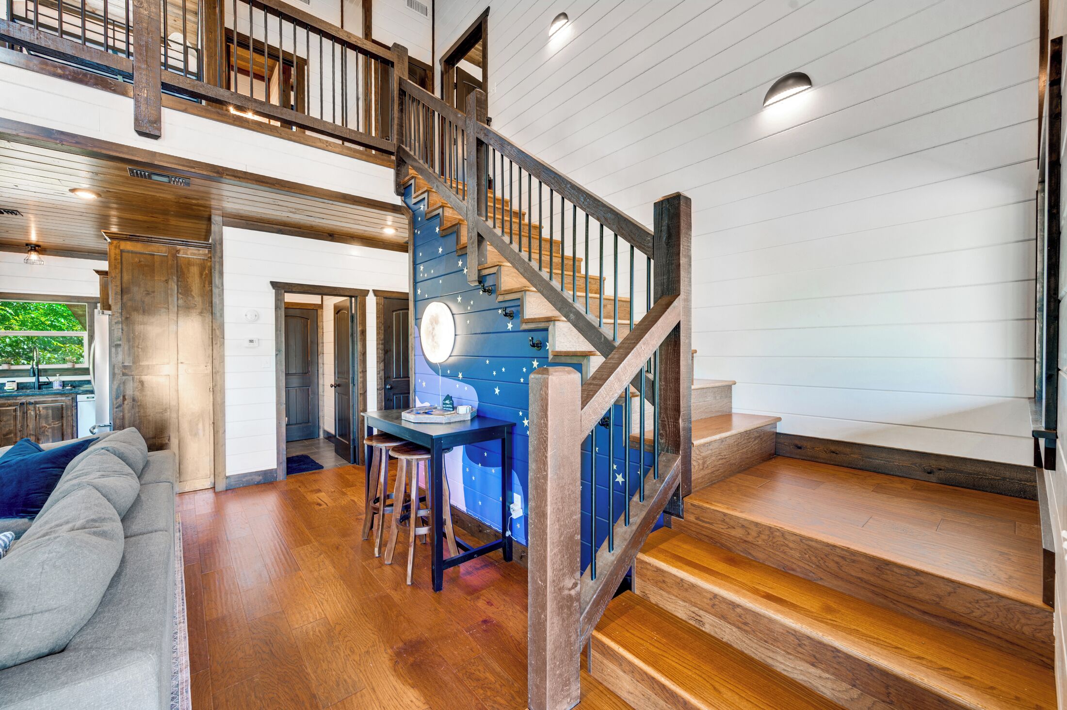 A spacious living area with a wooden staircase, a dining table with stools, and a blue accent wall with star decorations.