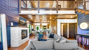 A spacious living room with a fireplace, a large gray sectional sofa, and a kitchen in the background. - Stargazing Dome, Hot Tub, Fire Pit, Luxury Cabin near Broken Bow (Broken Bow)