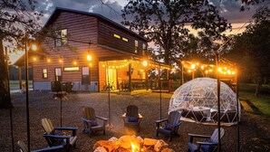 A rustic cabin with a fire pit and outdoor seating, surrounded by string lights. - Stargazing Dome, Hot Tub, Fire Pit, Luxury Cabin near Broken Bow (Broken Bow)
