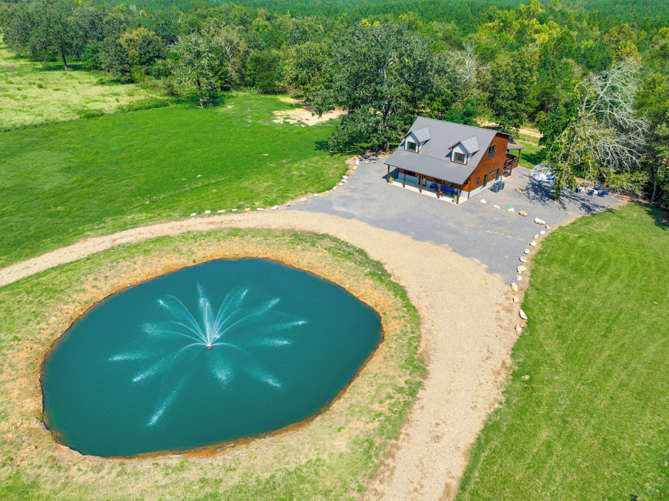 Ein Luftbild eines Hauses mit einem großen Teich, umgeben von einem gepflegten Rasen und Bäumen.