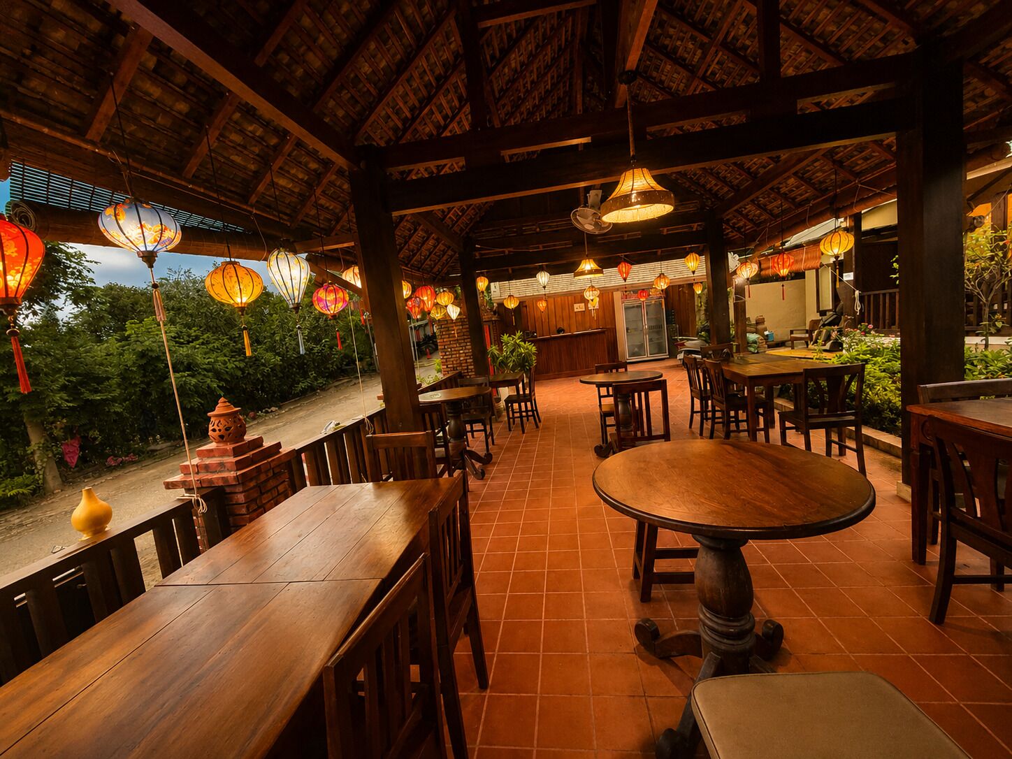 A restaurant with wooden tables and chairs, hanging lanterns, and a brick wall.