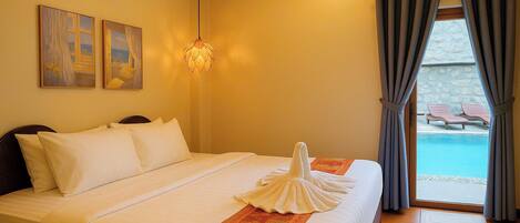 A hotel room with a bed, a painting, a hanging light fixture, and a view of a pool with lounge chairs.