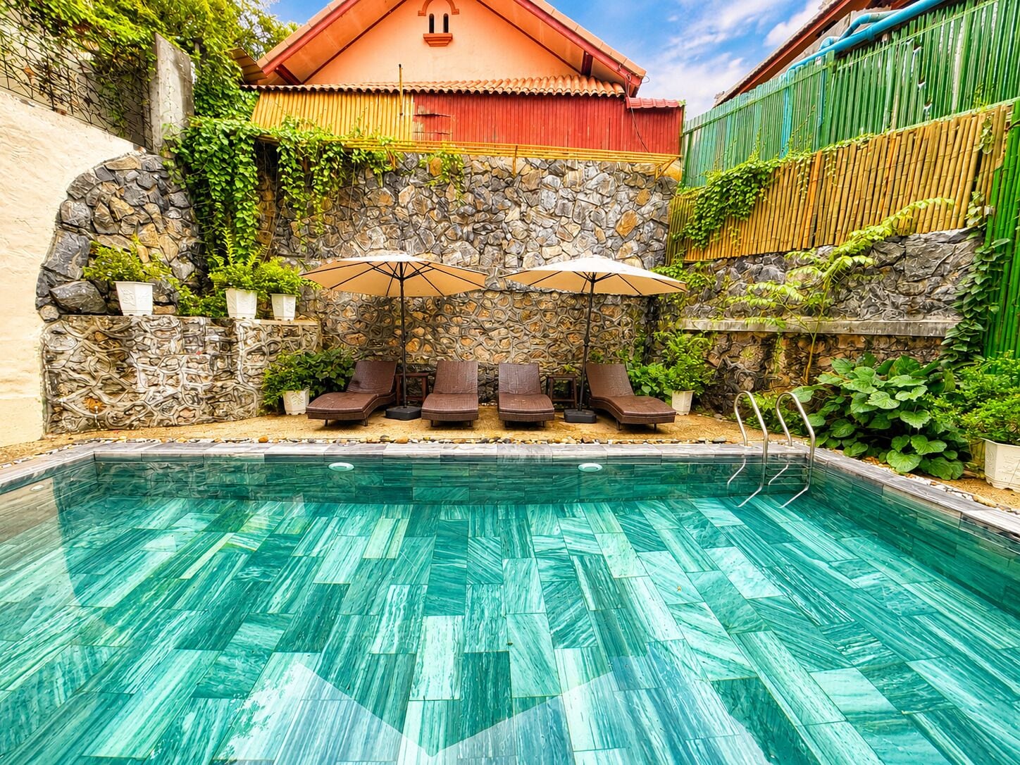 A swimming pool with lounge chairs and umbrellas, surrounded by stone walls and greenery.