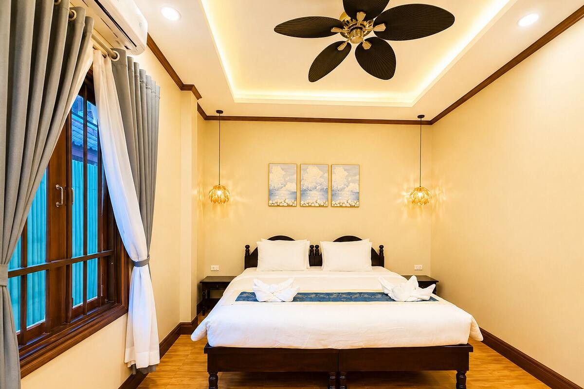 Hotelkamer met een bed, gordijnen, een plafondventilator, wandlampen en kunstwerken.
