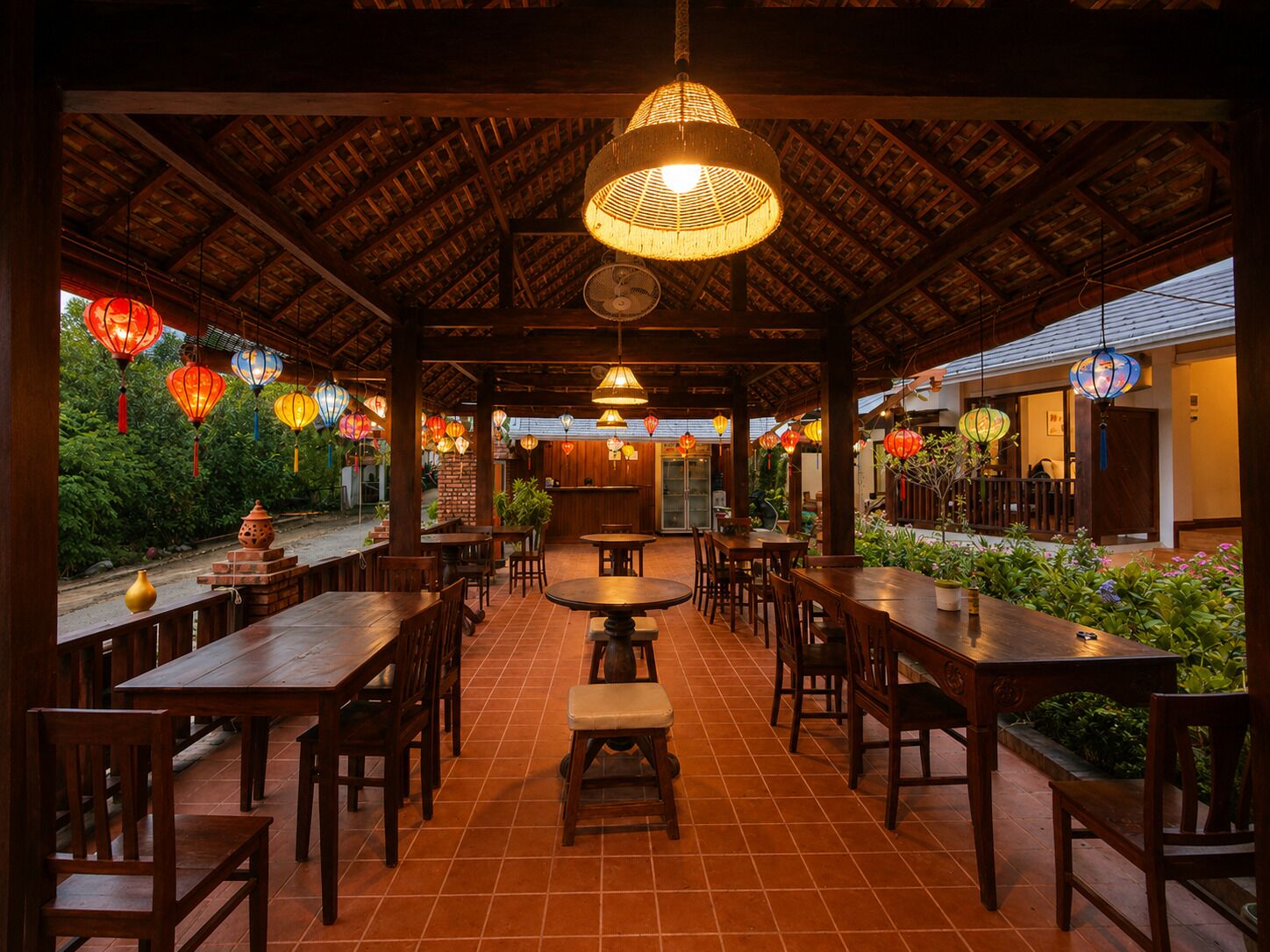 Un restaurant en plein air avec des tables et des chaises en bois, des lanternes suspendues et un sol carrelé.