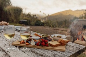 Una mesa de madera con una tabla de quesos, copas de vino y un cuenco de nueces.