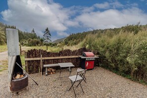 Un área de barbacoa al aire libre con una parrilla, una estufa de metal, una mesa y sillas.