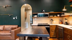 A modern kitchen with a wooden table, dark cabinetry, and a microwave above the counter. - Newly Renovated, Cozy Mid-Lake Cabin; Sleeps 10 (Many)