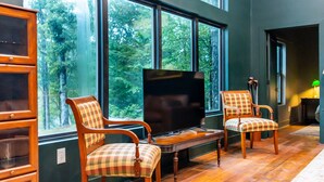 A room with large windows, a television, and two wooden chairs with checkered cushions. - Newly Renovated, Cozy Mid-Lake Cabin; Sleeps 10 (Many)