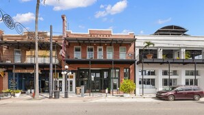 A street view with a brick building labeled 'SUGAR HOUSE' and a white building with a balcony.