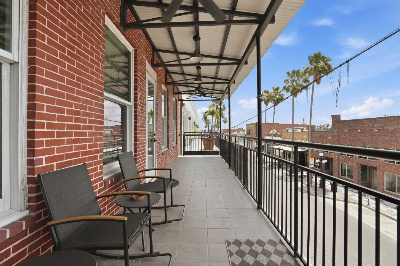 Ein Balkon mit zwei Stühlen und einem Tisch, ein Gebäude aus rotem Backstein und ein klarer Himmel.