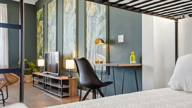 A hotel room with a bed, a desk with a lamp, a TV, and a chair.