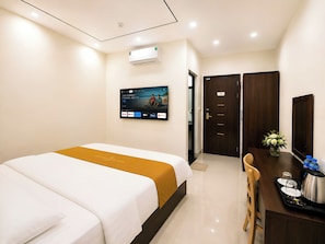 A hotel room with a bed, a desk with a coffee maker, a TV mounted on the wall, and a door leading to another room.