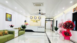 Eine saubere, moderne Hotelhalle mit Empfangsbereich, grüner Lounge und dekorativen Blumen.