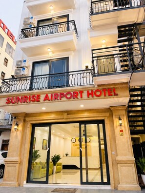Het uiterlijk van het Sunrise Airport Hotel, met een duidelijke ingang, een zichtbare receptie door de glazen deuren en een trap naar de verdiepingen.