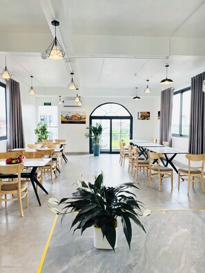 A spacious dining area with multiple tables and chairs, large windows, and hanging pendant lights.