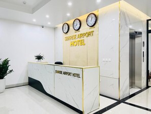 Een receptiebalie met klokken en de tekst 'Sunrise Airport Hotel'.