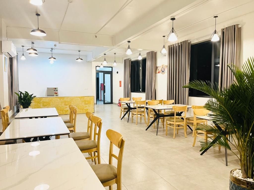 A spacious dining area with multiple tables and chairs, a reception desk, and a potted plant.